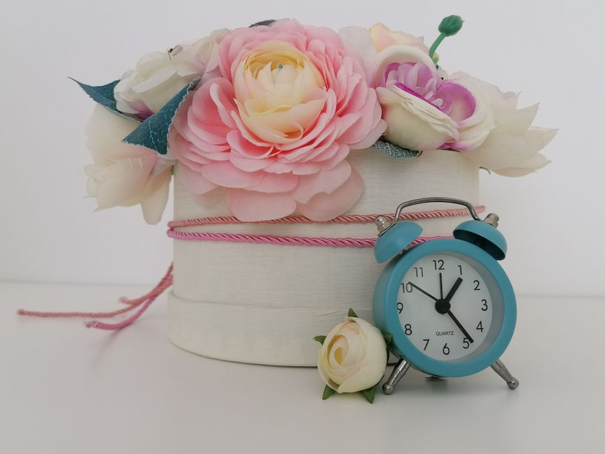 A floral arrangement featuring a variety of fresh artificial flowers in pastel shades, including pink and cream roses, peonies, and other blooms, all arranged in a round white gift box wrapped with pi