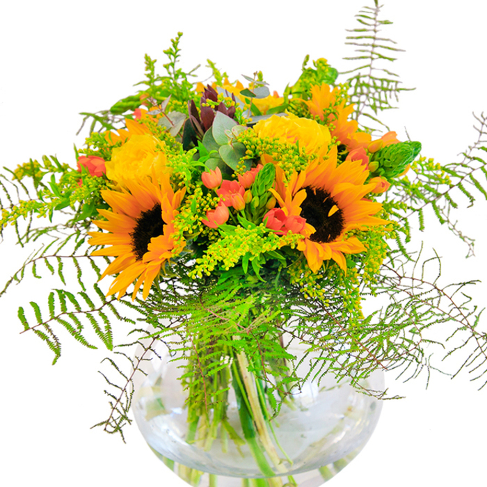 This Hook-inspired bouquet exudes sunlit exuberance, artfully composed of radiant sunflowers and buttery yellow roses cradled in a round glass vase. Each sunflower, with its dark brown heart and striking yellow-orange petals, conjures the image of late summer meadows that edge Hook's landscapes, while the tightly packed roses lend a timeless sophistication. Their petals unfold in soft, creamy spirals, intermingling seamlessly with clusters of shiny red Hypericum berries that glisten like jewels against the bouquet's lush greenery. Feathery fern fronds and sprigs of goldenrod breathe a sense of movement into the design, reminiscent of gentle breezes that sweep through Hook's parks and community gardens. Delicate flakes of bluish eucalyptus provide a cool, calming undertone. The transparent vase reveals a tangle of sturdy stems nestled in water, enhancing the arrangement's sense of freshness and vitality. From a close vantage, one can almost sense the subtle fragrance of open fields mingling with the crisp snap of green foliage. This arrangement, perfect as a celebratory gift or charming centerpiece, distills the warmth and optimism of Hook's welcoming community into every bloom, bridging heartfelt moments with local botanical artistry.