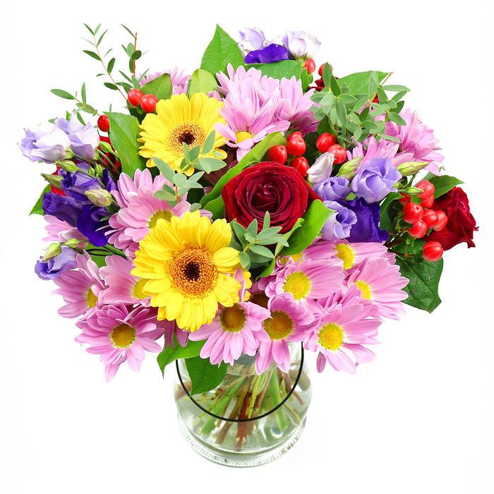 In this image, a large mixed bouquet rises confidently from a clear glass vase, its colours and forms standing out vividly against a white, uncluttered background. The arrangement is full and rounded, with deep red roses placed near the centre, their velvety petals unfurling in layered spirals that add depth and a hint of timeless romance. Beside them, bright yellow gerberas with warm brown-orange centres bring a bold, sunny energy, echoing the friendly, village feel of Hook and its surrounding lanes. Encircling these focal flowers, clusters of soft pink daisies or chrysanthemums spill outward, their numerous fine petals forming a feathery halo around small yellow middles. These pink blooms lend a soothing, approachable softness to the composition, reminiscent of cottage gardens tucked away off London Road. Woven through the pinks and yellows, you can see elegant stems of lisianthus in purple and pale lavender, their bell-shaped blossoms and gently ruffled edges adding cool tones and a sense of refined movement. Scattered among the flowers, shiny red hypericum berries stand out on their slim stems, offering round pops of texture that break up the petals and draw the eye from one part of the bouquet to another. A variety of greens anchors the design-broad, darker leaves near the base, with lighter, finer foliage lifting the top and edges-creating a fresh, natural frame that suggests living hedgerows. In the transparent vase, neatly aligned stems and clear water speak of expert preparation and freshness, as though the flowers have just arrived from an early-morning delivery. The overall impression is of a joyful, welcoming bouquet, ideal as a centrepiece for a family gathering in Hook, a birthday surprise, or a heartfelt gesture to brighten someone's day.