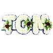 This image features a traditional name tribute spelling TOM in large capital letters, crafted as a funeral flower arrangement and displayed against a bright, uncluttered white background. Each letter is built on a sturdy frame and completely covered with tightly massed white chrysanthemums, forming a thick, plush surface that looks almost like freshly fallen snow. A rich royal blue ribbon is carefully pinned around the outer edge of every letter, its satin sheen and neatly pleated folds adding structure, polish, and a respectful formality often chosen for memorial arrangements in the Hook area. At three focal points across the design-the top corner of the T, the gentle curve of the O, and the upper side of the M-the calm white sea of blooms is interrupted by clusters of accent flowers. These small arrangements combine deep crimson-red roses, soft white or cream spray roses, and slender white freesia-like blooms, all nestled into pockets of glossy greenery and delicate fern fronds. The colour contrast of red, white, blue, and green symbolises love, purity, remembrance, and peace, making the tribute feel both meaningful and visually balanced. The letters rest on a single dark metal bar, keeping them aligned and steady, ready to be placed on a hearse, by the altar in a local church, or near the front of a crematorium chapel. The overall design radiates quiet dignity and personal affection, a bespoke floral memorial that speaks gently of the family's love for Tom and their wish to say farewell with beauty and care.